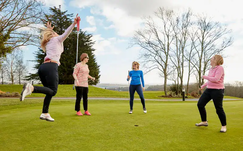 Women golfers joyously celebrating a successful putt on the course.
