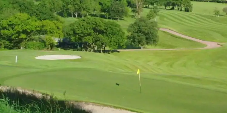 Dean Wood Golf Club Society Golf Day Deals This image shows a smoothly contoured putting green in the foreground, bordered by a bunker, with gently rolling fairways and another bunker visible further back.