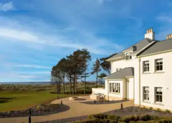 Dunluce Lodge: Five-Star Luxury on the Edge of Royal Portrush A large white house with a golf course and trees.