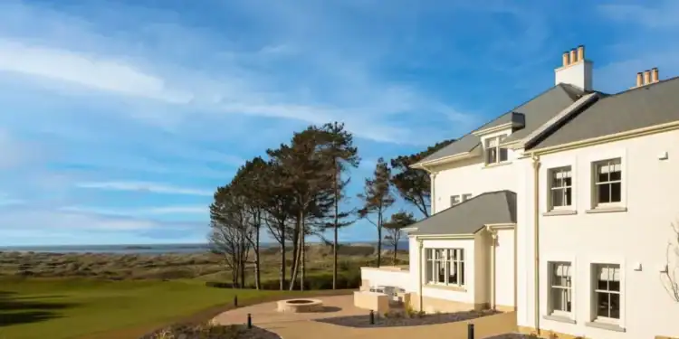 Dunluce Lodge: Five-Star Luxury on the Edge of Royal Portrush A large white house with a golf course and trees.