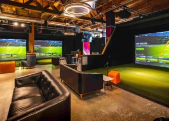 Five Iron Golf to Open Indoor Golf Venue in Riyadh in 2026 A room with a large golf simulator screen and a couch.