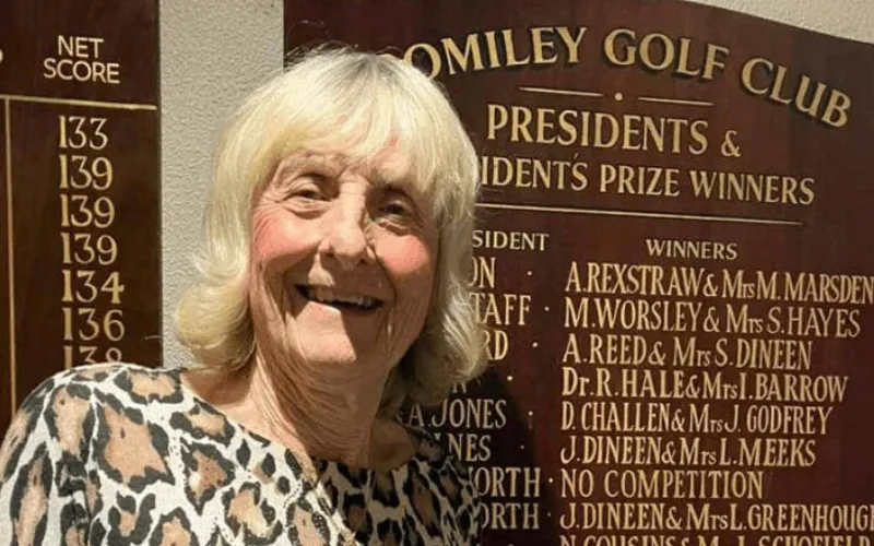 Romiley's Janet Godfrey Shoots 49 Points at 80! Romiley’s Janet Godfrey smiling in front of a plaque.