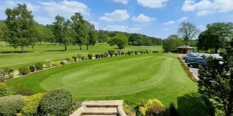 Romiley's Janet Godfrey Shoots 49 Points at 80! a large green lawn with cars parked in the back