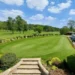 Romiley's Janet Godfrey Shoots 49 Points at 80! a large green lawn with cars parked in the back