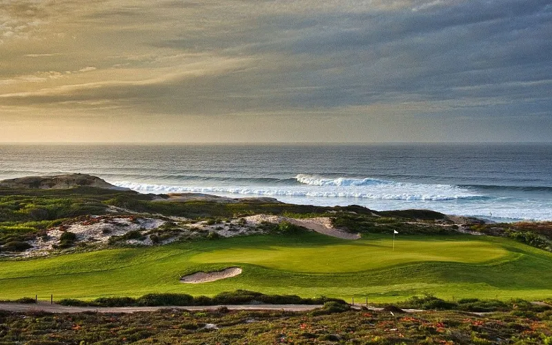 Marriott Praia D’El Rey Golf & Beach Resort a golf course with a flag on the beach with Pebble Beach Golf Links in the background