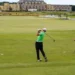 Golfer swings on lush green course.